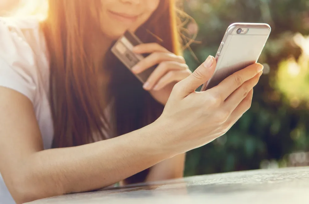 girl looking at cell phone with credit card in hand