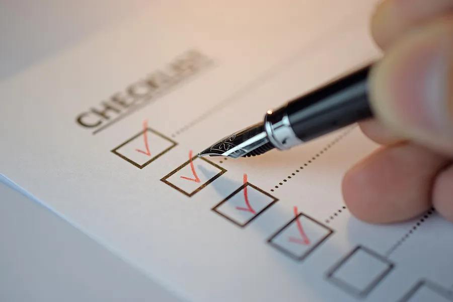 Close-up of a hand using a pen to check off items on a checklist, representing an old phone testing checklist for battery, performance, and security.